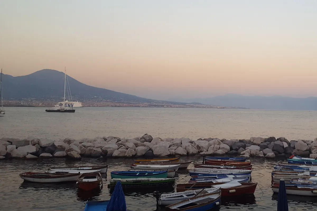 Small rowing boats in a harbour at dusk with Mount Vesuvius across the Bay of Naples