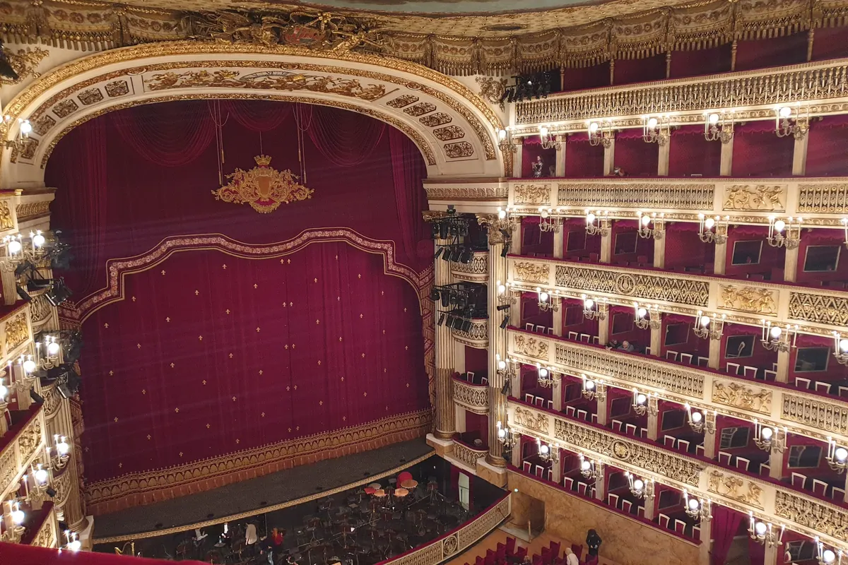 The red-and-gold auditorium of the Teatro di San Carlo seen from a high gallery, with the stage curtain closed